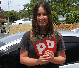 Young female student standing by driving school vehicle showing P plates