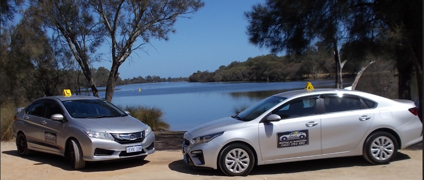 Two Ability Drive silver colour Driving school cars, parked facing each other, with river in the background