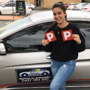 Young female student standing next to driving school car showing 2 P plates after passing driving asseesment