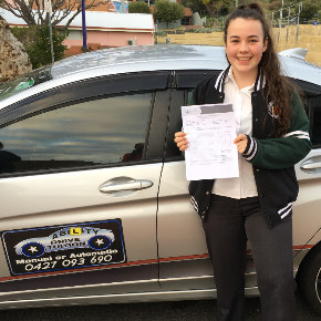 Female student standing next to driving school car showing driving licence form after passing her driving test